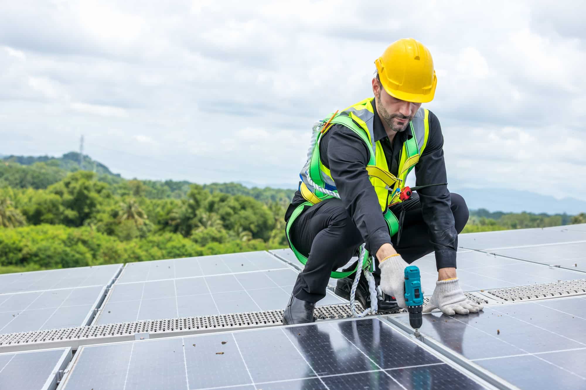 a man in a yellow hard hat using a drill to install solar panels